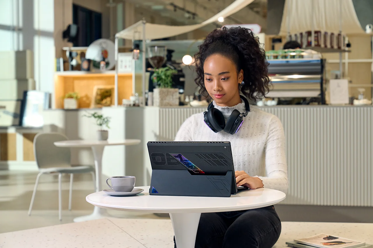 A young person using an ASUS Flow laptop in a café, showing its sleek design and portability.