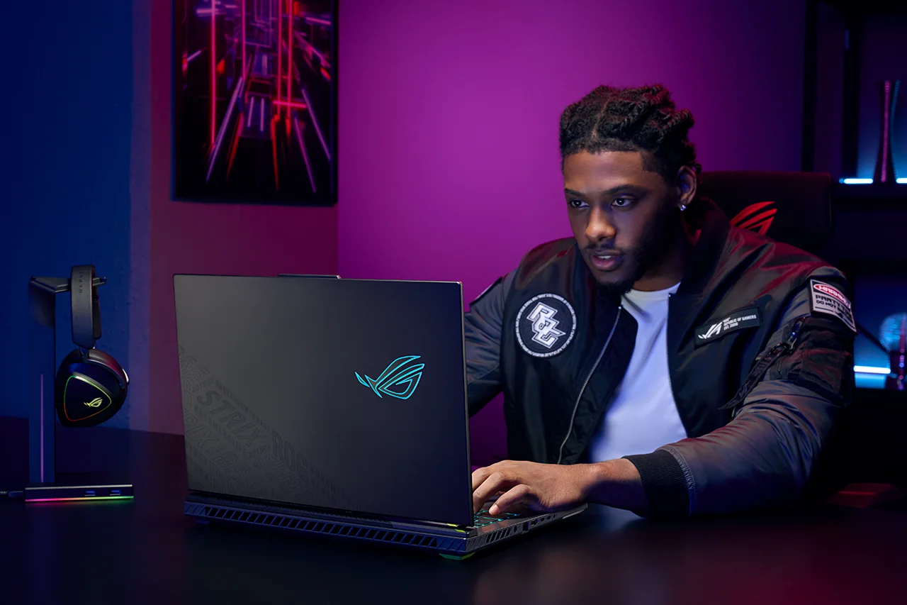 An avid gamer playing games on the ASUS ROG Strix laptop in a vibrant gaming setup, showcasing its illuminated logo and premium accessories.