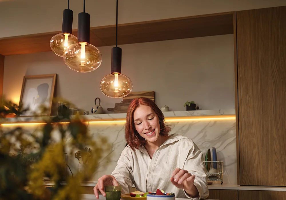 Warmly lit kitchen with Philips Hue pendant bulbs, modern wood cabinetry, and natural greenery.
