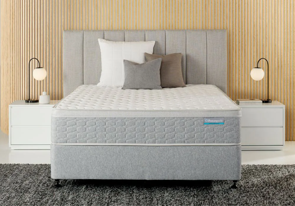 Modern bed with grey upholstered headboard, layered pillows, white nightstands, and lamps against vertical wood panelling.