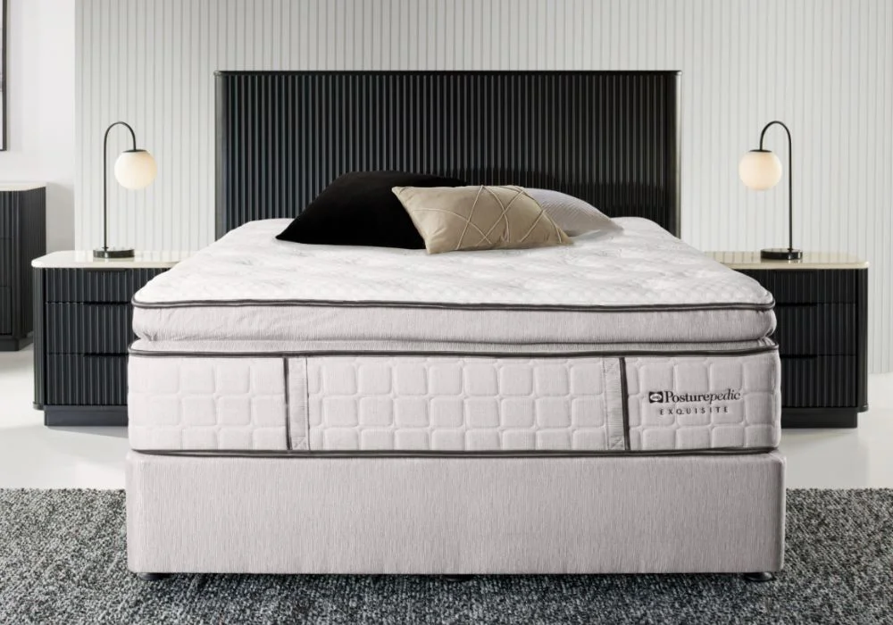 Posturepedic Exquisite mattress on a textured, silver mattress base with black and beige pillows, dark headboard, and lamps on matching nightstands.
