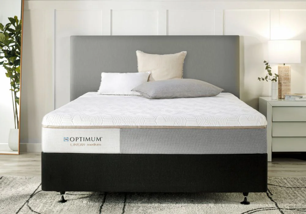 Modern bedroom with grey upholstered headboard, Optimum Linear Medium mattress, and neatly styled white-grey pillows