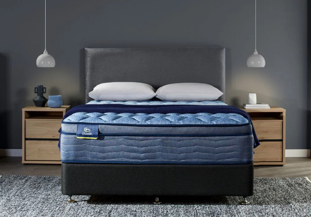 Serta Classic mattress on a stylish bed with blue quilted cover, white pillows, and modern nightstands in a calm, grey-toned bedroom.