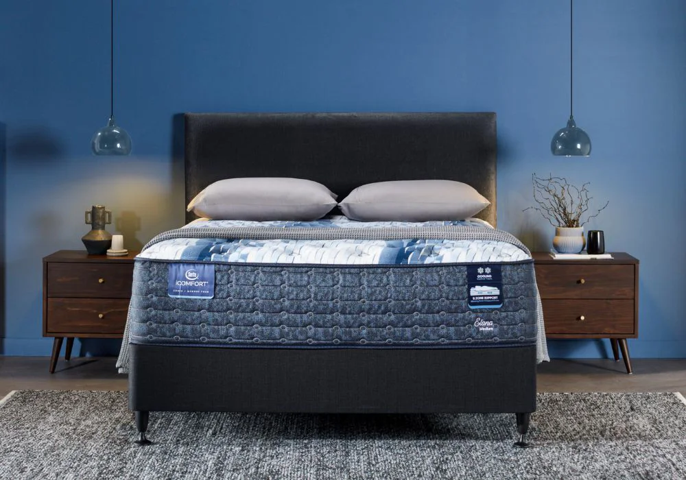 iComfort by Serta mattress with blue and grey quilted design on a bed frame with matching bedside cabinets on either side holding ornaments, in a stylish bedroom.
