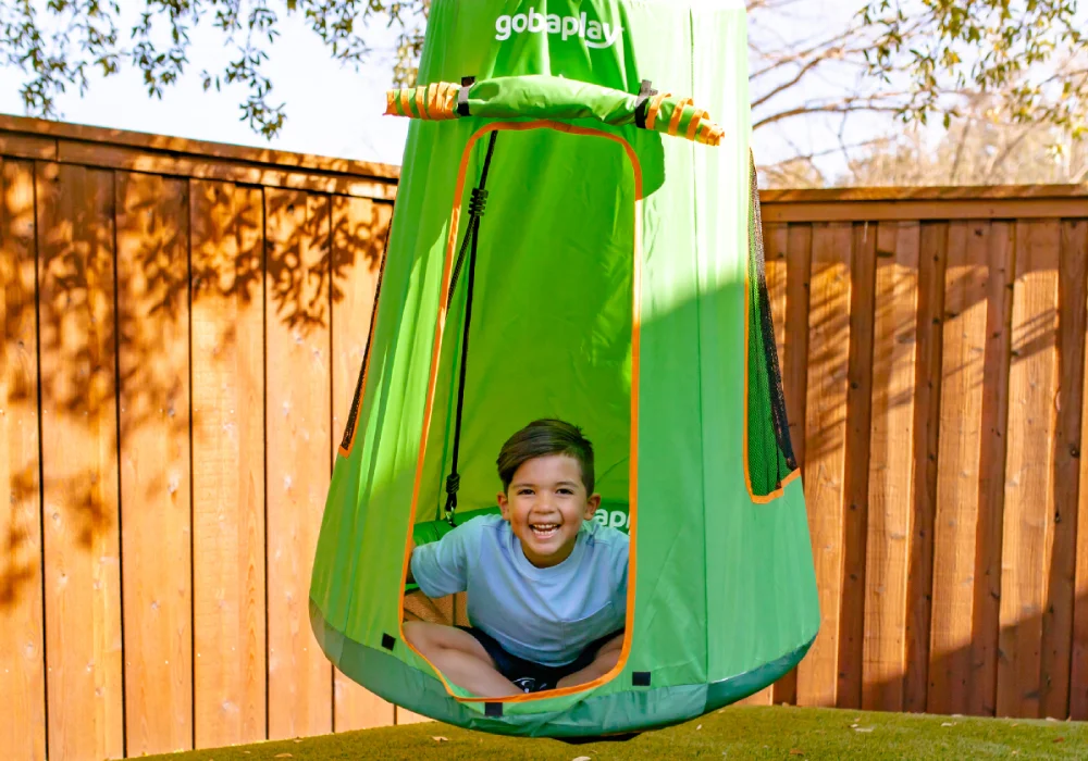 Four children playing on a green geometric climbing dome structure with triangular panels and orange connectors, set in a grassy outdoor area.