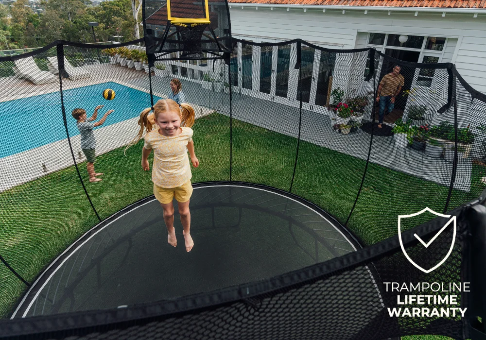 Child jumping on a trampoline in a backyard with a pool and house in the background; text reads 'Trampoline Lifetime Warranty'.