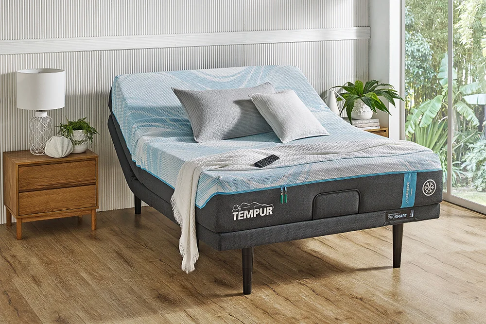 A tempur Breeze mattress, on a bed frame in a bedroom with a window and plants in the background.