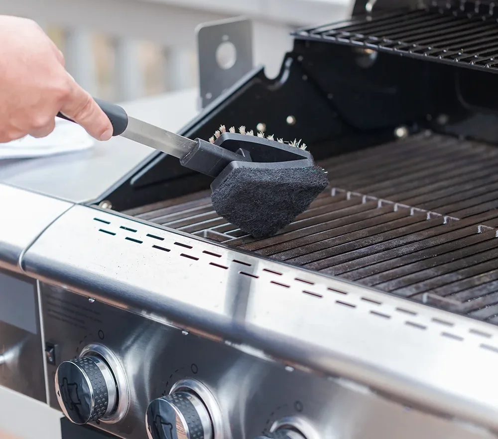 Close-up of a clean black BBQ grill with a person lifting the main grate, revealing a multi-level cooking surface including an upper warming rack.
