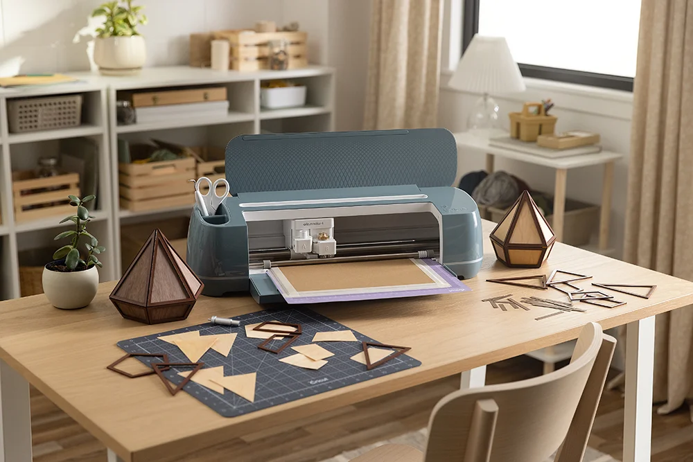 A cricut maker 4 machine on a craft room table with various shapes cut out on the table.