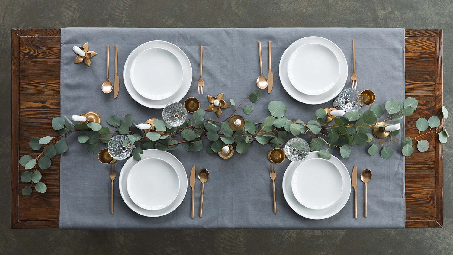 Top view of rustic table setting with eucalyptus, tarnished cutlery, wine glasses, candles and empty plates on tabletop 