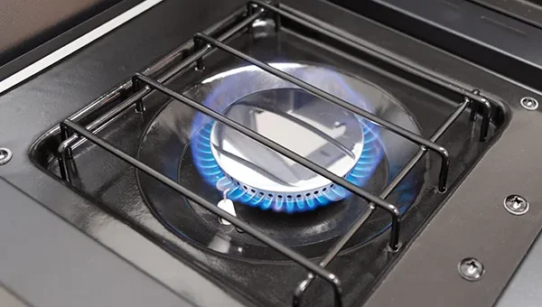 Close-up of Gasmate Quasar BBQ's side burner with active blue flame beneath a metal grate.