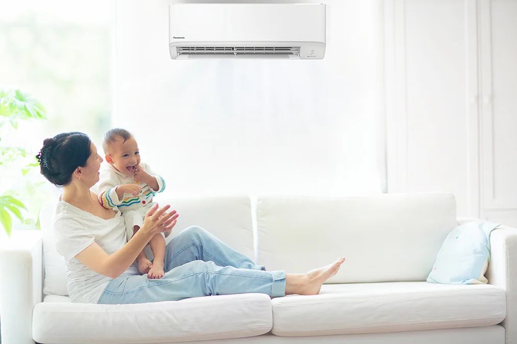 Happy mum and baby relaxing on the couch with a Panasonic heat pump running in the background.