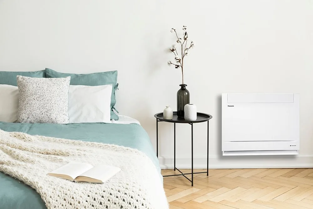 A Panasonic floor console installed on the wall of a bedroom at ground level, on the left is a simple bedside table with some ornaments.