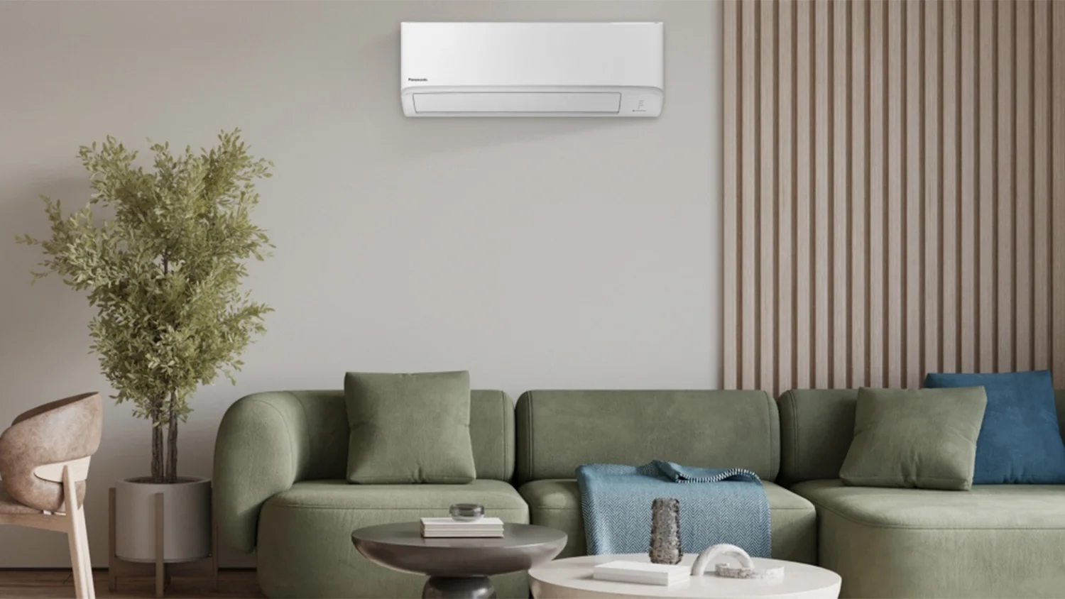 A Panasonic high wall Aero Series heat pump on the wall behind a green 3-seater modular couch in a modern living room.