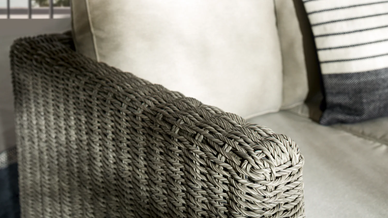 Close-up of resin wicker armrest on the Mercedes outdoor lounge suite with beige cushions and striped accent cushion, showcasing woven texture and craftsmanship.