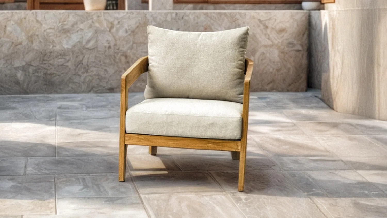 Ferrera teak wood outdoor lounge chair with light cushions on a tiled floor, styled in a minimalist setting in a stone patio.