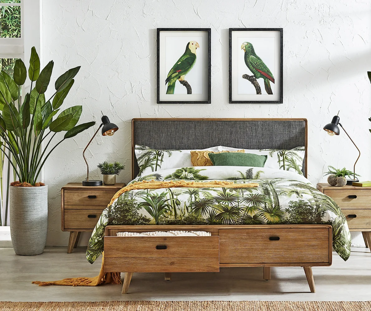 The queen-size, Braga bed frame with drawers, with a drawer open, in a bedroom styled with natural elements. Matching bedside tables from the Braga collection sit on either side of the bed, along with matching bedside lamps and some ornaments.