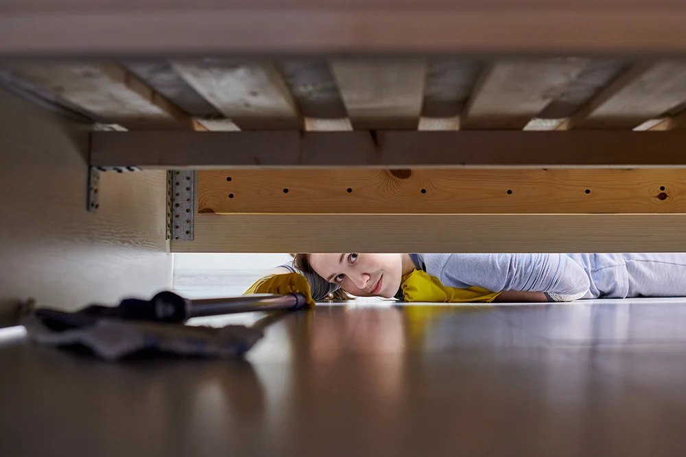 A lady diligently cleaning the floor with a mop while peeking under.