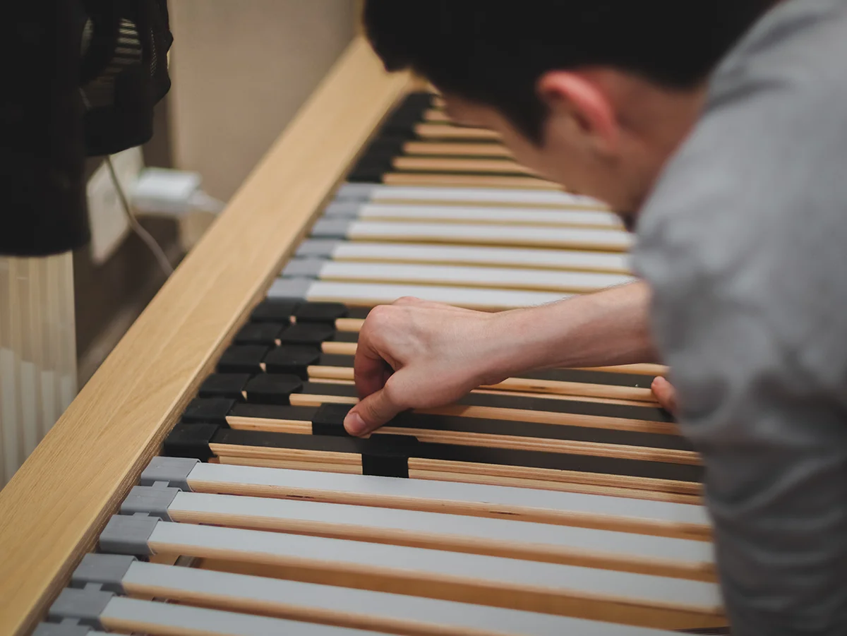 A close up photo of a guy fixing the frame slats into the plastic mounts of a bed frame.