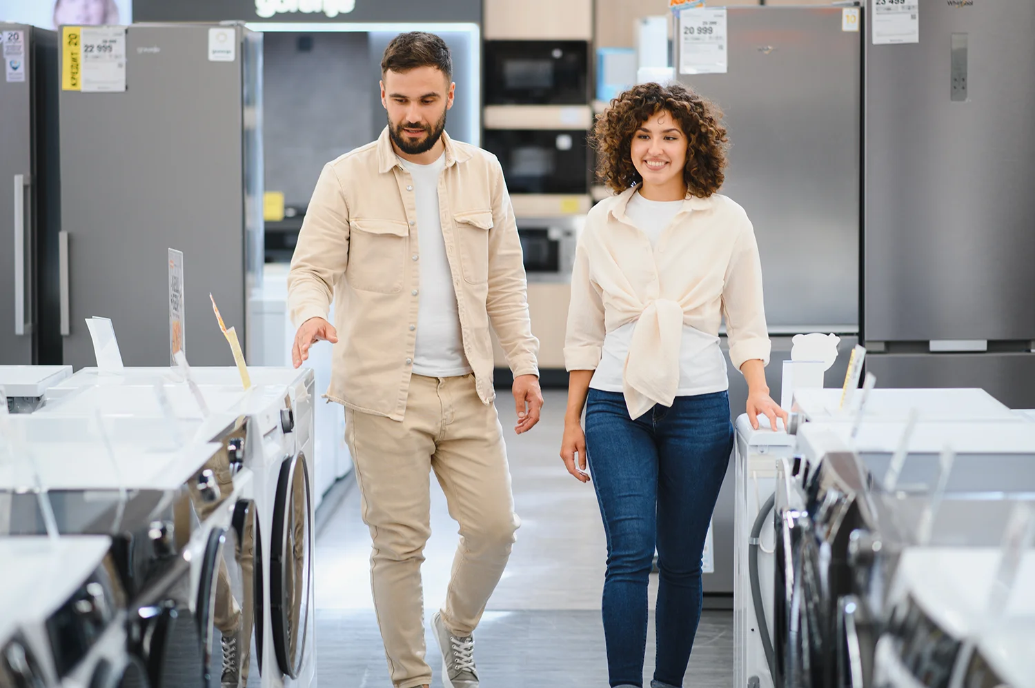 A lady with short brown hair in an orange sweater with both hands raised and palms facing up against a solid light blue background, appearing to present or compare something.