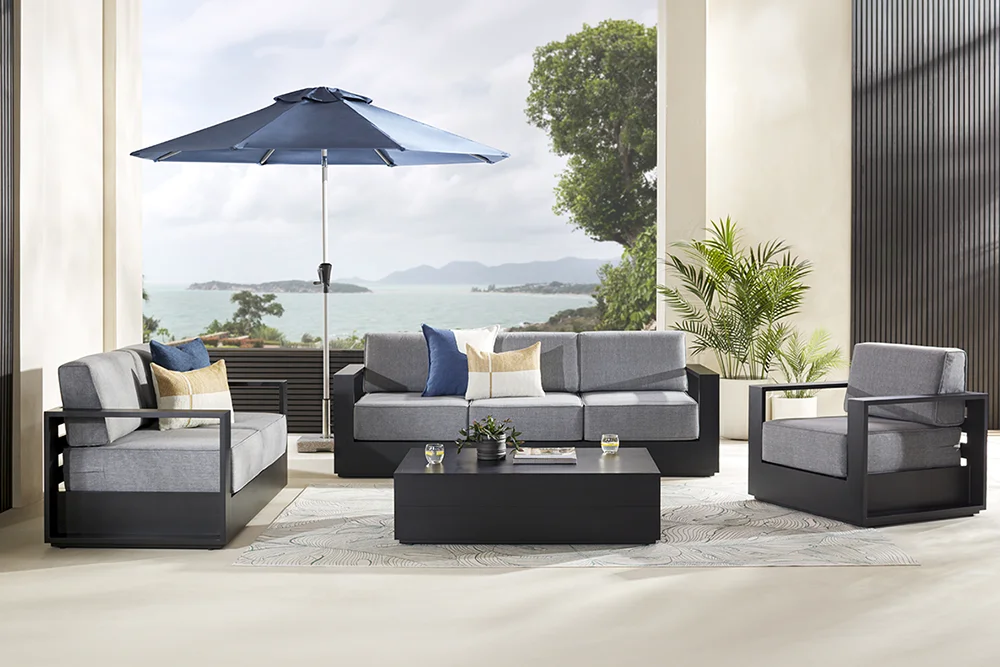 Coastal outdoor lounge setting with cream sofa, armchairs, ottomans and coffee tables overlooking the ocean.