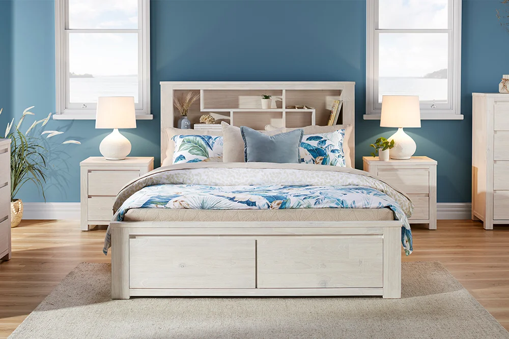 Coastal-style bedroom featuring the Palm Beach Storage Queen Bed Frame, styled with white, beige and blue bedding, decorative pillows, matching Palm Beach bedside tables with voluptuous bodied white lamps on top.