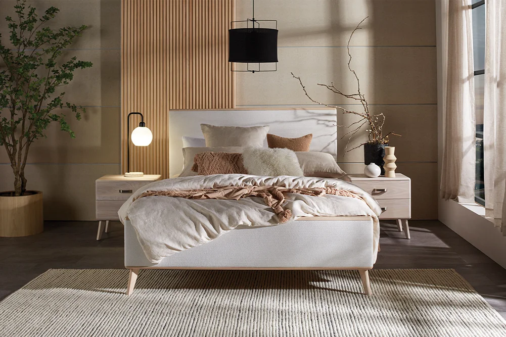 Contemporary organic bedroom with the Melba Queen Bed Frame by Woodpecker Furniture, styled in neutral tones with textured pillows, wooden bedside tables, modern lamps, and a large potted plant by tall windows.